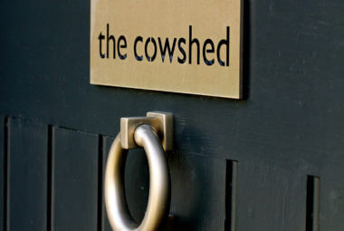 a blue barn conversion front door with knocker and sign saying the cowshed