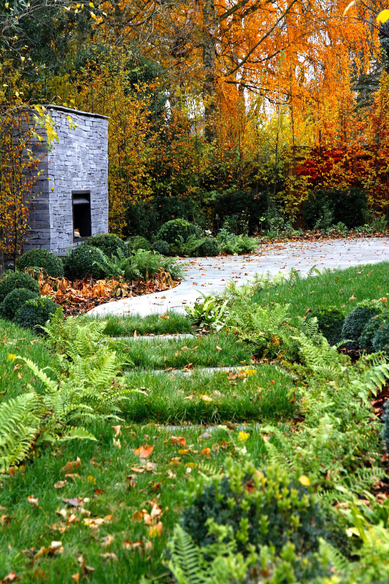 landscaped garden in September with outdoor fireplace and orange and yellow foliage and fallen leaves