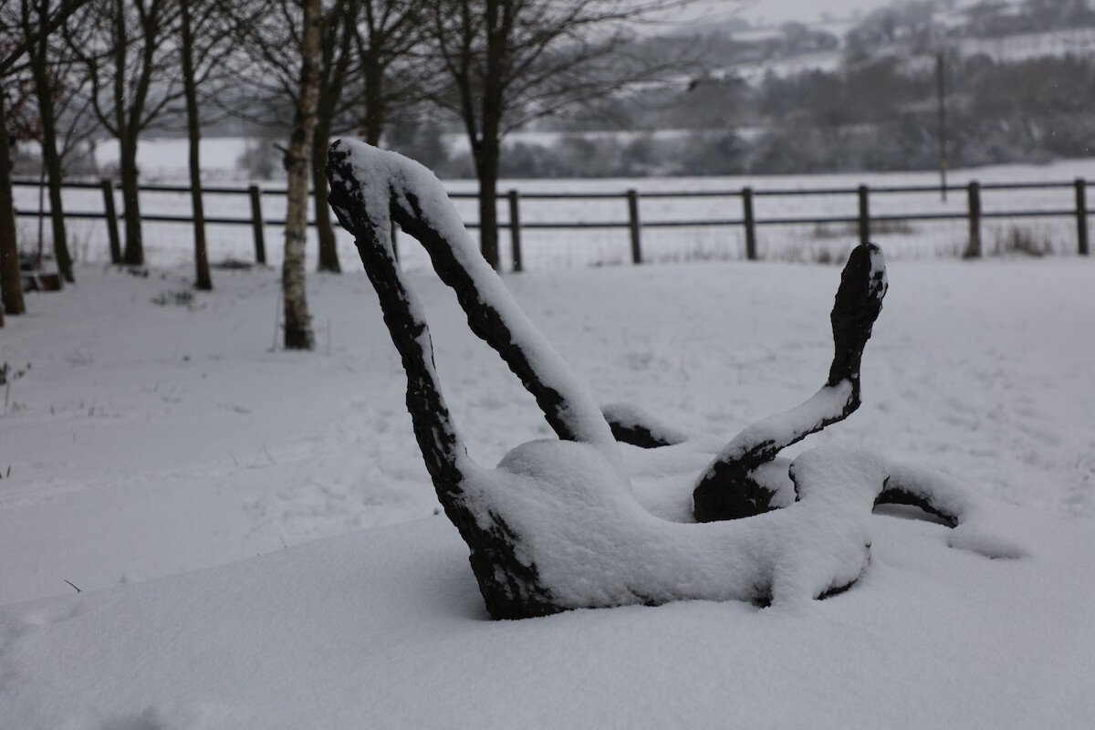 a bronze landscape sculpture of a dog rolling in the snow in the cotswolds