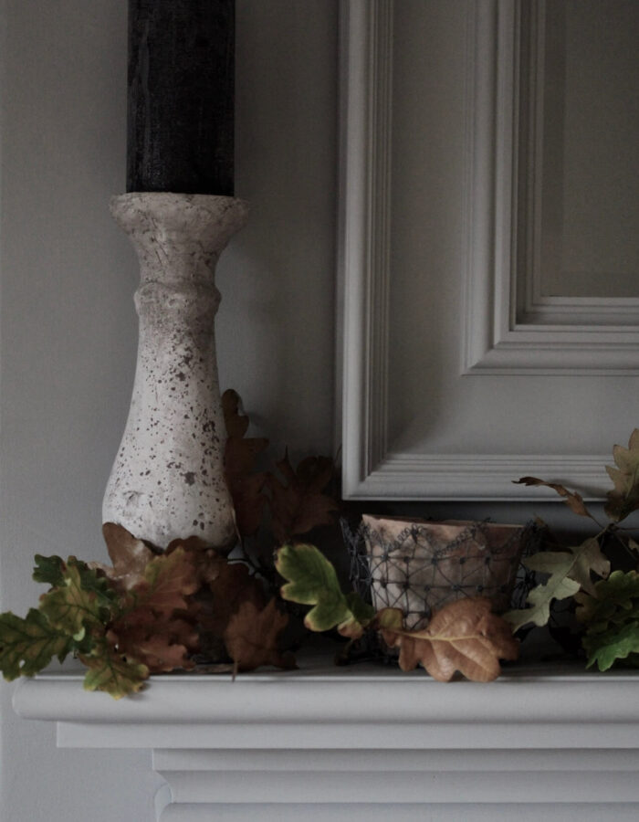 a mantlepiece painted in Farrow & Ball paint with Autumn leaves arranged around a stone candlestick and blue candle