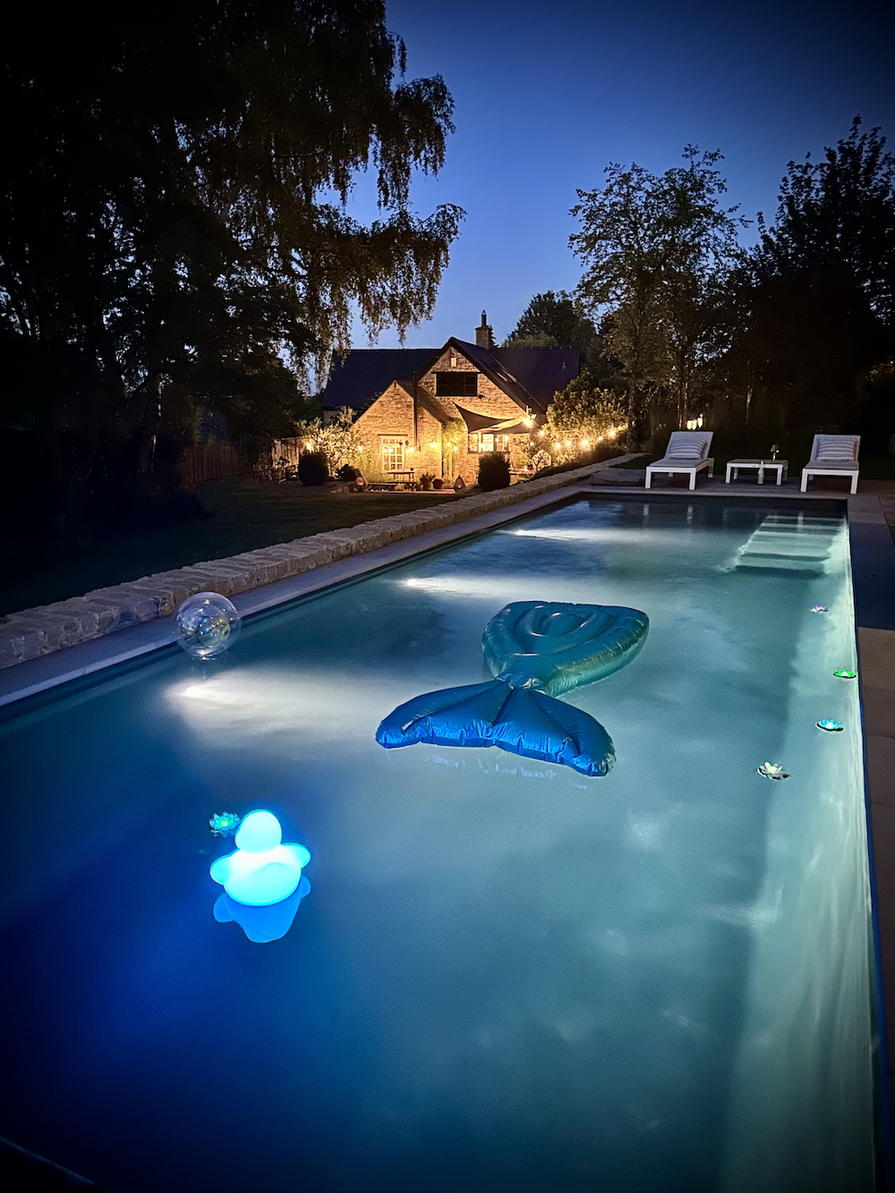Swimming pool by night in poolscape garden with inflatables floats near by Soho Farmhouse 